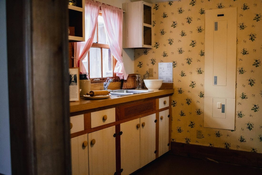 A vintage kitchen with floral wallpaper, cabinets, and a sink